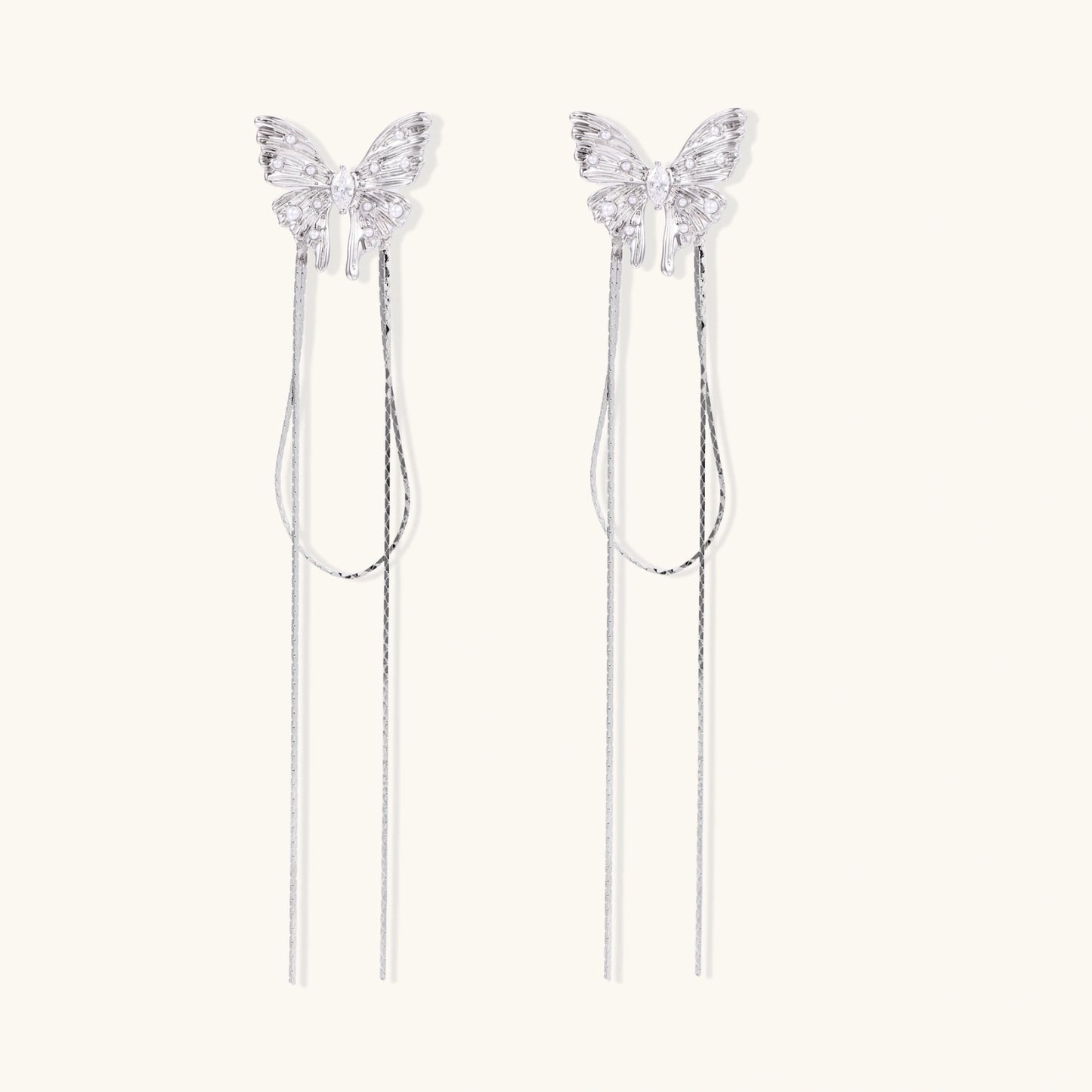 Pair of silver threader earrings with crystal butterfly tops and long chain drops on cream background.