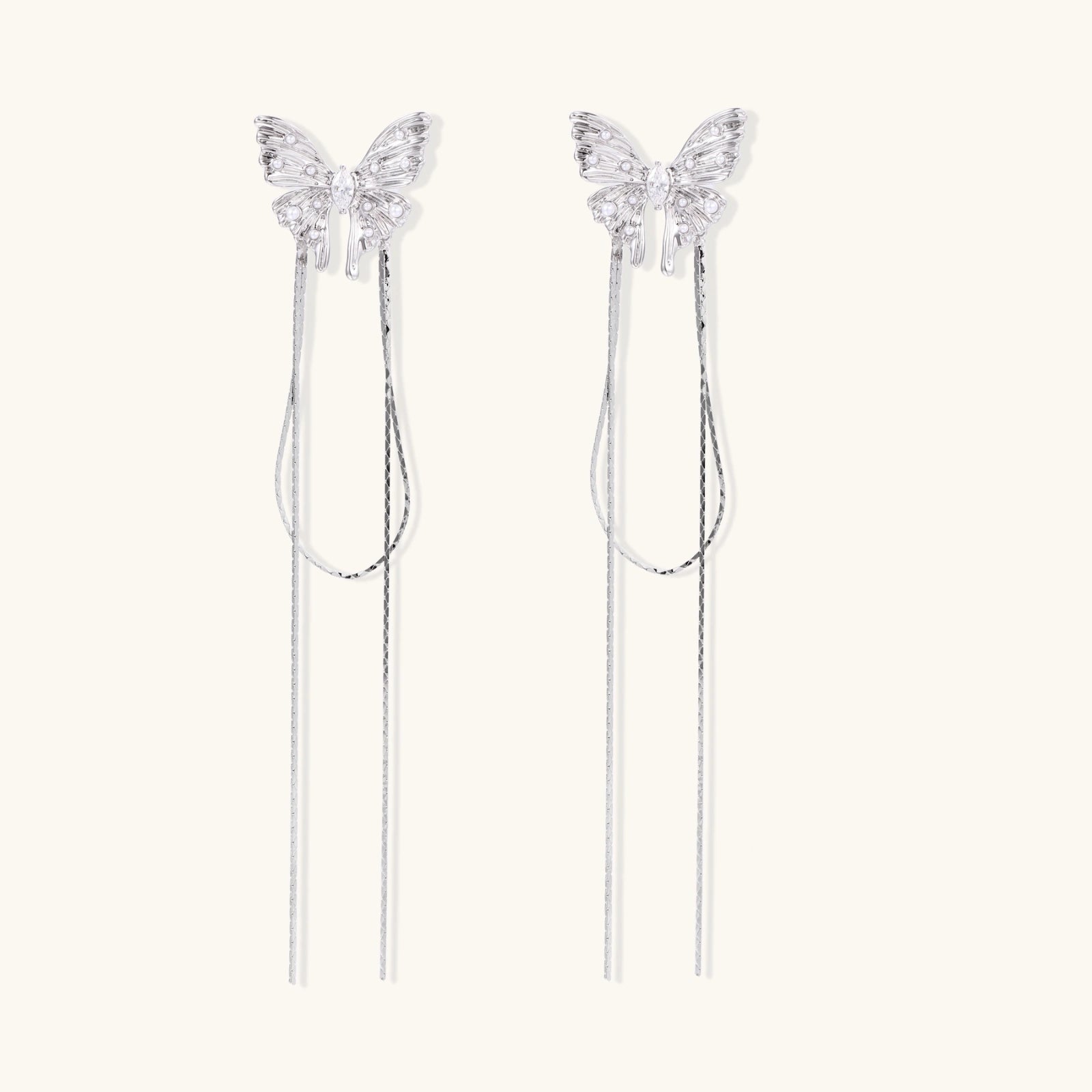Pair of silver threader earrings with crystal butterfly tops and long chain drops on cream background.